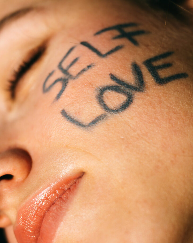 Nahaufnahme eines Gesichts mit dem Schriftzug Self Love auf der Haut
