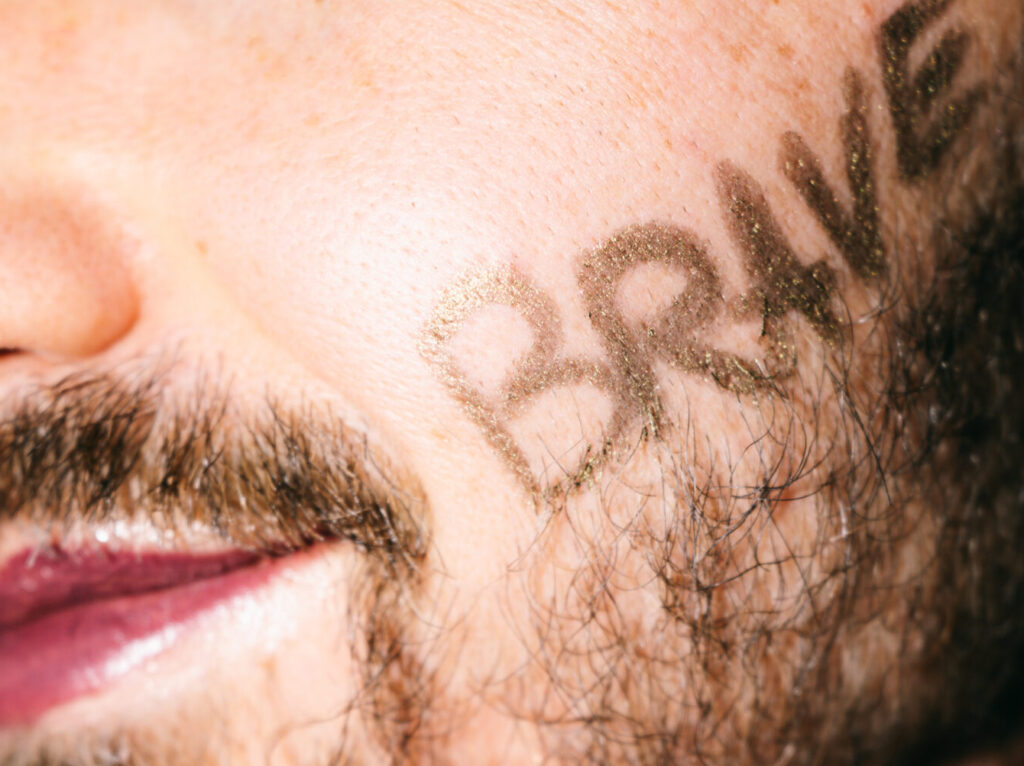 Nahaufnahme eines Gesichts mit dem Schriftzug Brave auf der Haut
